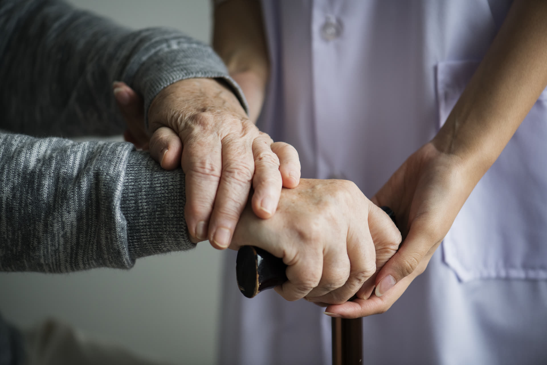 Close-up of a caregiver and senior resident holding hands on a cane
