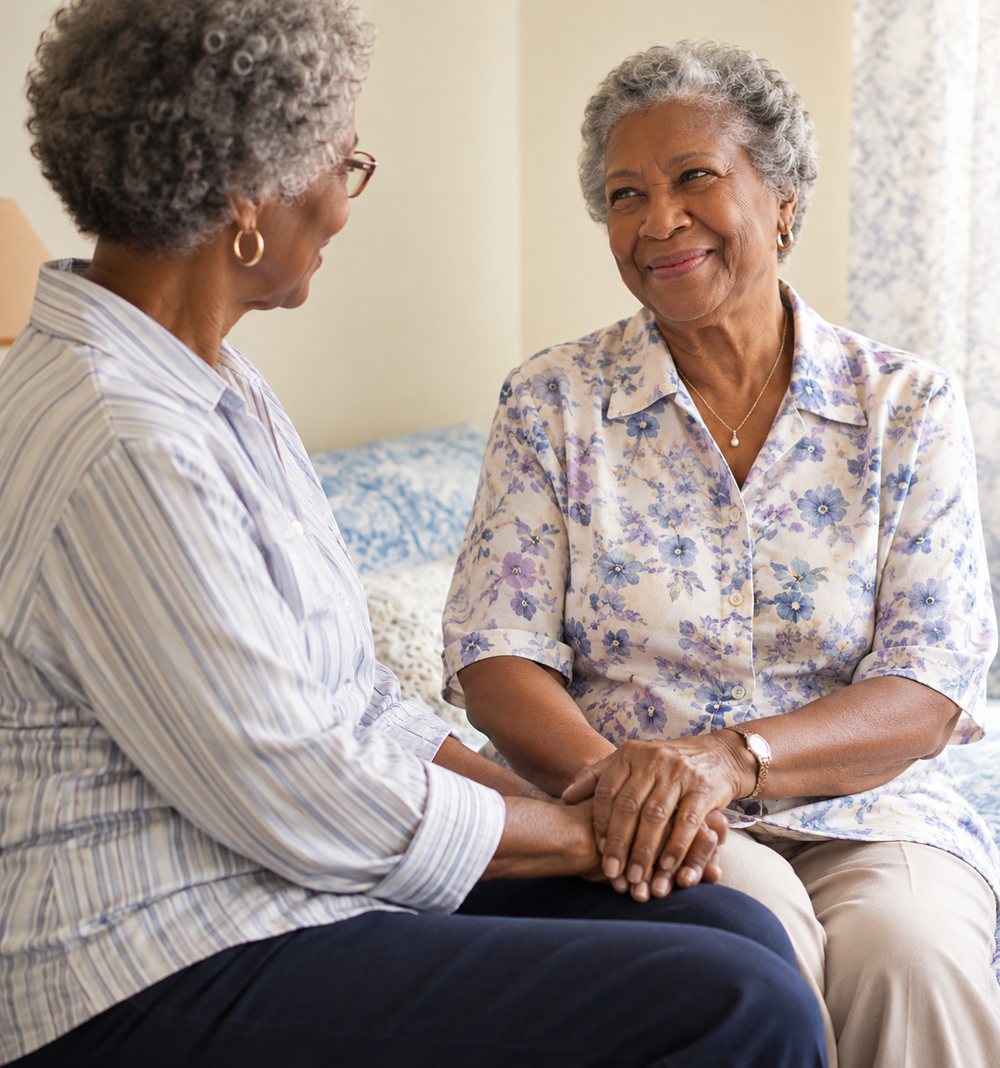 Two senior friends sitting together on a bed, holding hands and talking