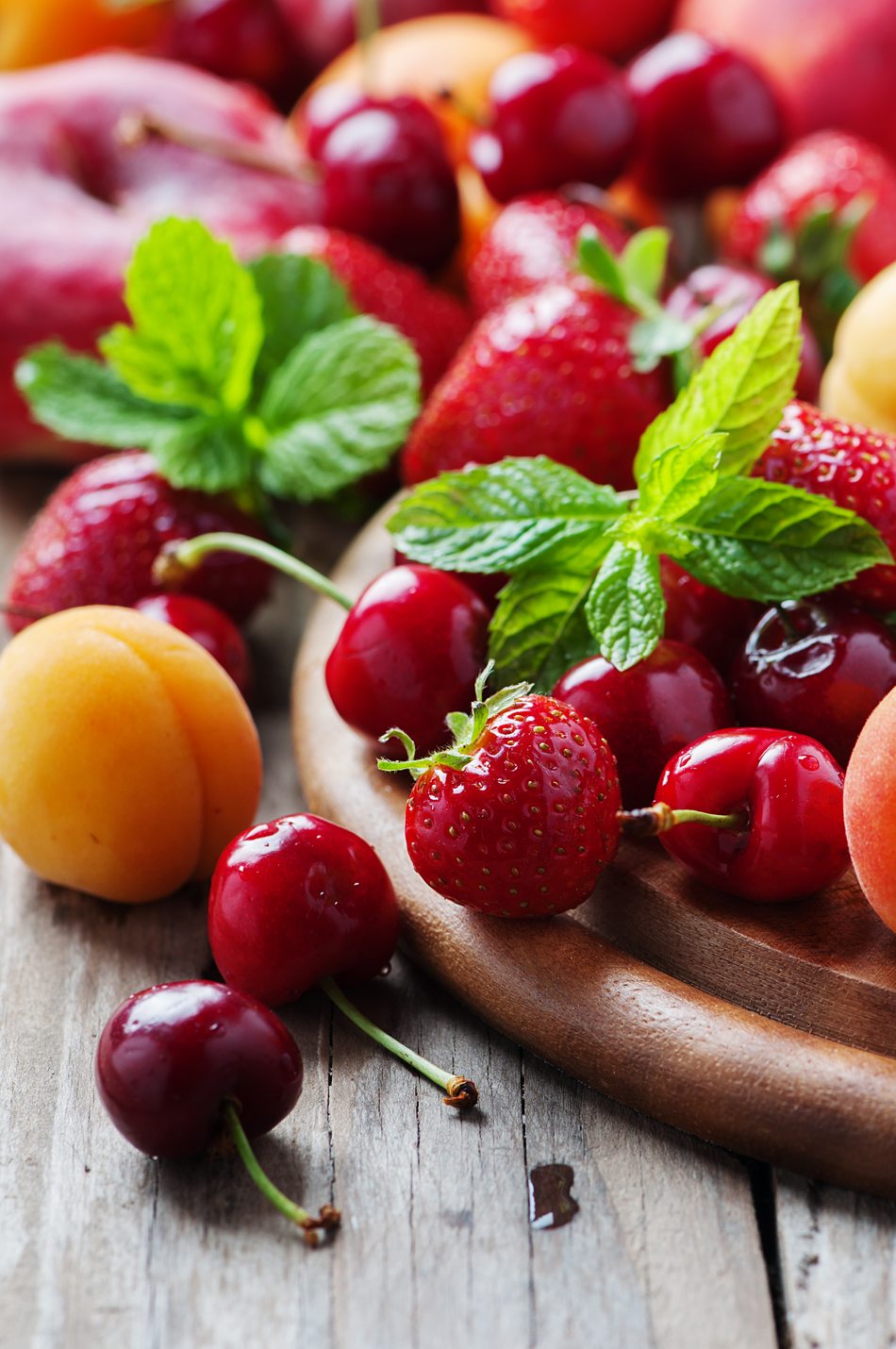 Strawberries, cherries and apricots with fresh mint on a wooden board