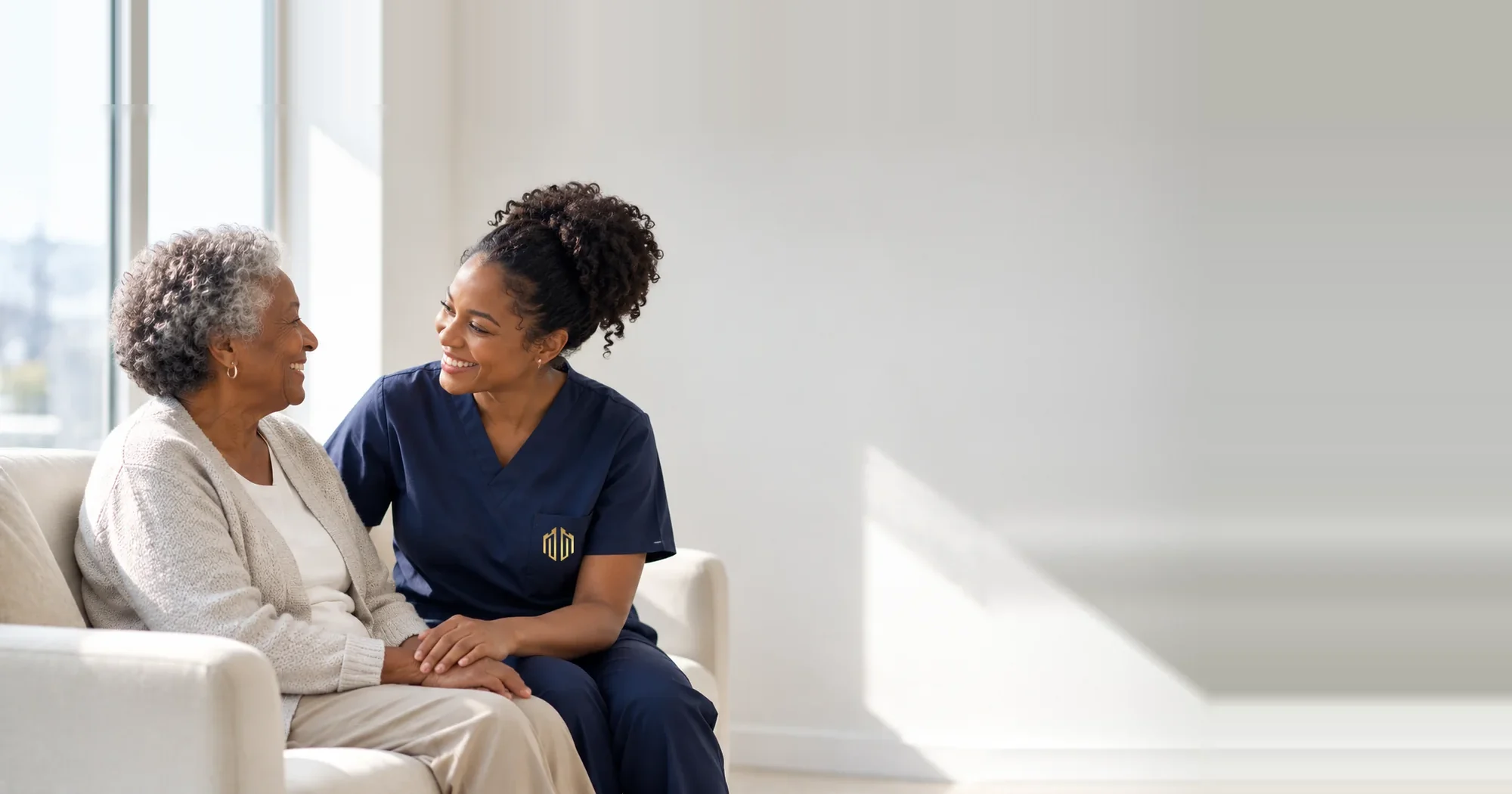 A nurse sitting with a resident in a sunlit lounge, the two of them smiling at each other